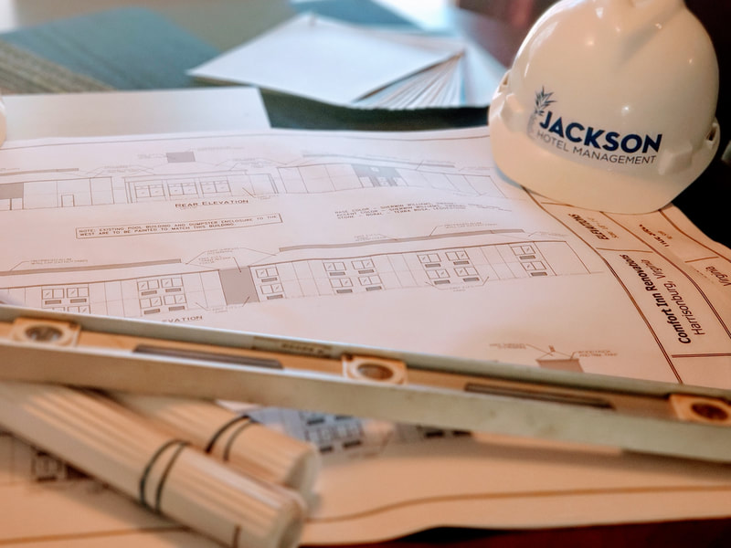 Picture of building plans with a hard hat with the Jackson Hotel Management logo on it